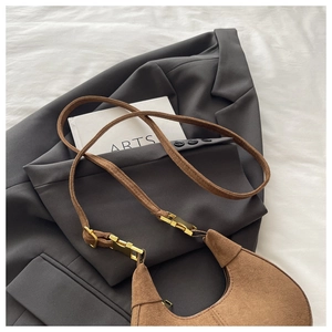 Détail du sac demi-lune en daim marron avec boucle dorée sur un blazer gris chic