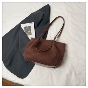 Détail du sac cabas en daim marron café avec poignées en cuir lisse sur tissu blanc