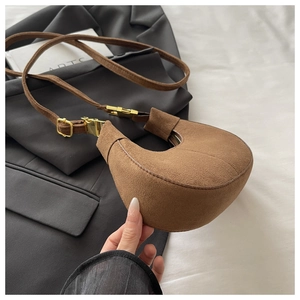 Détail d'un sac demi-lune en daim marron avec garnitures dorées sur fond blanc et noir