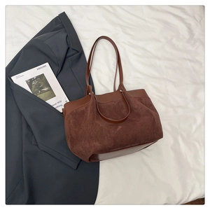 Détail d'un grand sac cabas marron en daim et cuir posé sur un blazer gris et magazine