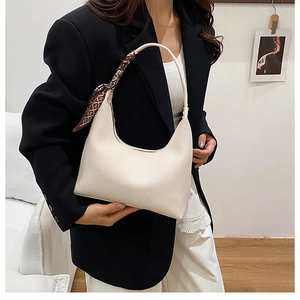 Close-up of a creamy white crescent bag with lychee grain texture and a decorative silk scarf