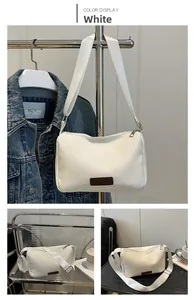 Detail view of white nylon crossbody bag with silver zipper and brown leather label