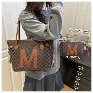 Detailed view of the large brown tote bag and matching clutch with M-letter pattern