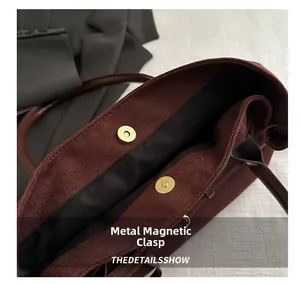 Detailed close-up of golden magnetic buckle on vintage burgundy suede tote bag