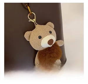 Detail of knitted teddy bear charm with plush pom-pom and gold keychain on leather bag