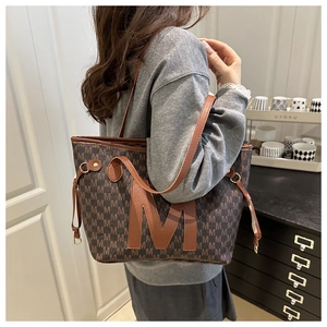 Deep brown tote bag detail with letter M pattern and leather shoulder strap on model