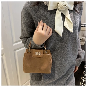 Detail of tan suede small tote bag featuring golden metal twist lock and leather piping