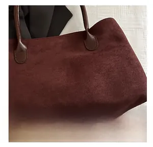 Detailed close-up showing burgundy suede texture and brown leather strap of the tote bag