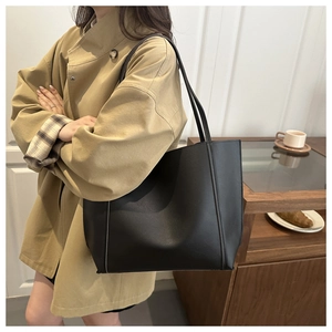 Minimalist black matte leather tote bag shown on model in a cozy cafe setting