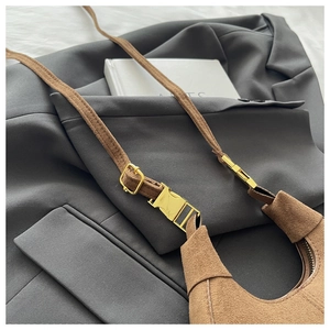 Gros plan du sac croissant en daim marron avec boucle en métal doré sur veste grise