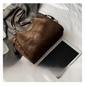 Close-up of brown suede tote bag with metal ring detail next to a tablet and blazer