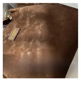 Macro shot of dark brown suede tote bag featuring stitched leather tag and gold metal ring