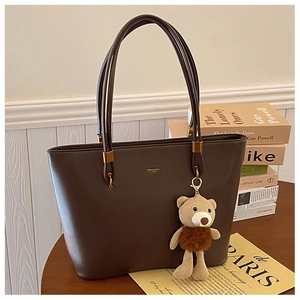 Detail view of large dark brown leather tote with gold logo and cute bear charm pendant