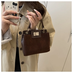 Detail of a brown leather square handbag showing the golden twist lock and suede texture