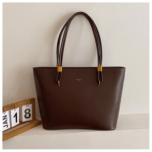 Detailed close-up of dark brown leather tote bag with gold logo and delicate twin straps