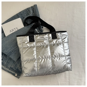 Detail of silver quilted tote bag with metallic finish and black woven strap handles