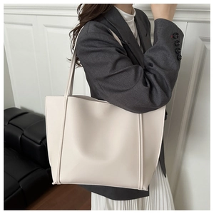 Lifestyle view of a large cream tote bag worn with a grey blazer and pleated skirt