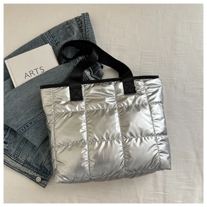 Close-up of metallic silver quilted tote bag with black strap on casual background