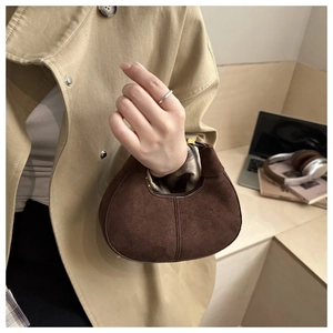 Détail d'un mini sac à main en daim marron foncé mat tenu par un mannequin en trench