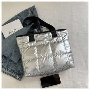 Detail of silver quilted tote bag with metallic texture and black fabric handles