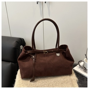 Close-up of a coffee brown suede tote bag with leather straps on a beige knit surface
