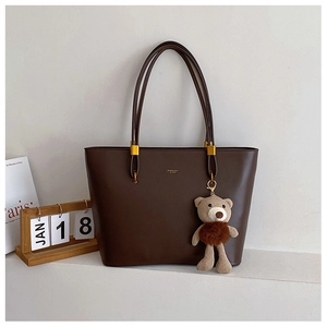 Detail of dark brown tote bag with gold rings and a cute teddy bear charm
