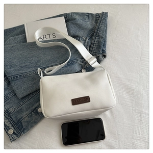 Close-up of small white crossbody bag with fashion label and adjustable wide strap