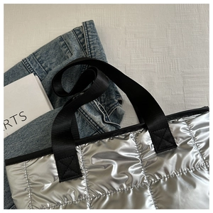 Detail of silver quilted tote bag with metallic texture and reinforced black nylon handles