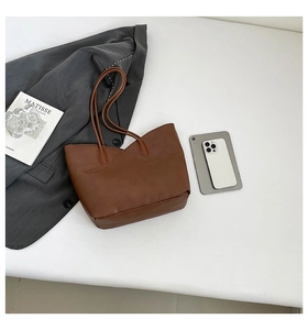 Flat lay of brown lychee leather tote bag with gray suit and tablet on white background