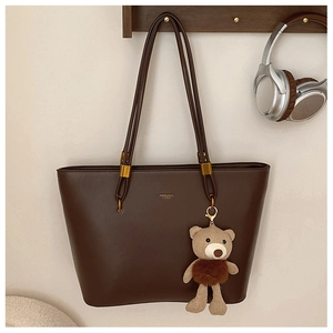 Detail of vintage brown tote bag with gold branding and a cute knitted bear charm