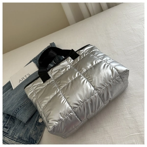 Detail of silver quilted puffer tote bag with black nylon handles on a stylish background