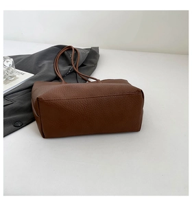 Close-up of brown lychee grain leather tote bag with long straps on white surface