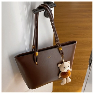 Close-up of vintage brown PU tote bag with gold hardware and a cute plush bear charm