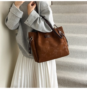 Detail of dark brown suede tote bag with drawstring metal rings and logo on side