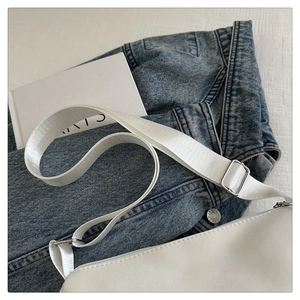 Detail of white crossbody bag with nylon strap and silver hardware on denim jacket