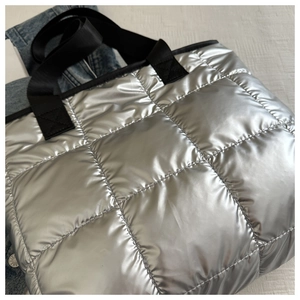 Close-up of silver quilted tote bag with metallic texture and black woven handles