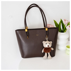 Detail of dark brown tote bag featuring golden hardware and a cute teddy bear charm