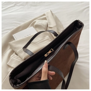 Detail of dark brown suede tote bag featuring a gold zipper and smooth leather straps
