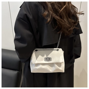 Détail du sac crème à chaîne avec fermoir strass porté sur un manteau noir élégant