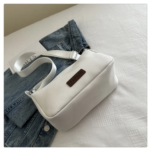 Detail of white canvas crossbody bag featuring brown leather FASHION patch and adjustable strap