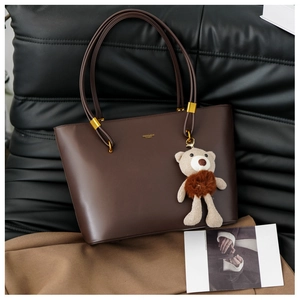 Detail of dark brown tote bag featuring golden F&K logo and a plush teddy bear charm