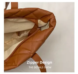 Detail shot of the secure zipper closure and beige lining on a brown quilted tote bag