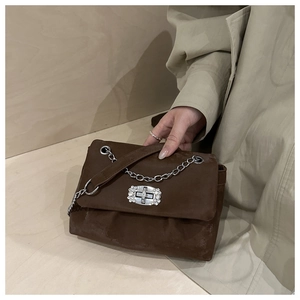 Close-up of dark brown suede handbag featuring a silver chain strap and jeweled buckle