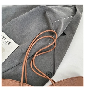 Detail of brown litchi pattern leather tote bag and grey twill blazer with white stitching