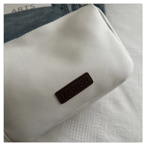 Close-up of white canvas bag with embossed brown leather FASHION label and zip closure