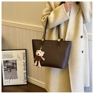 Detail of a dark brown PU tote bag with a plush bear charm on a beige wool coat
