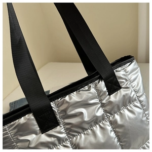 Close-up of metallic silver quilted texture and black woven handles on this handbag