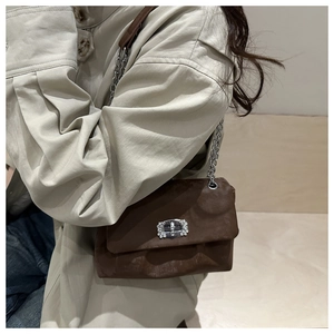 Close-up of brown suede ruched bag with silver rhinestone buckle and chain strap