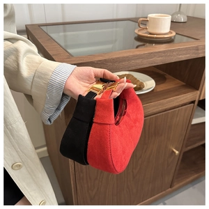 Detail of red and black suede half-moon bags with gold metal buckles in a lifestyle setting