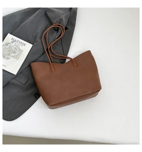 Top view of brown lychee texture leather tote bag with Matisse book and suit on white desk